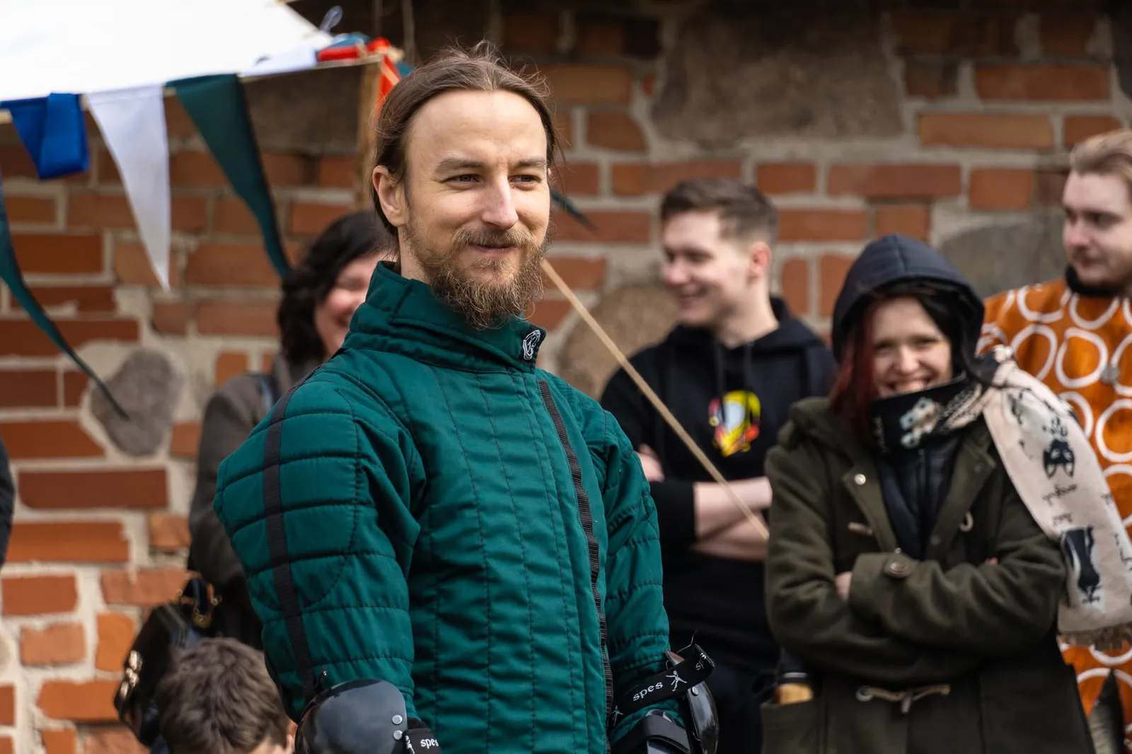 Smiling fencer in a green gambeson in front of a brick wall at an event