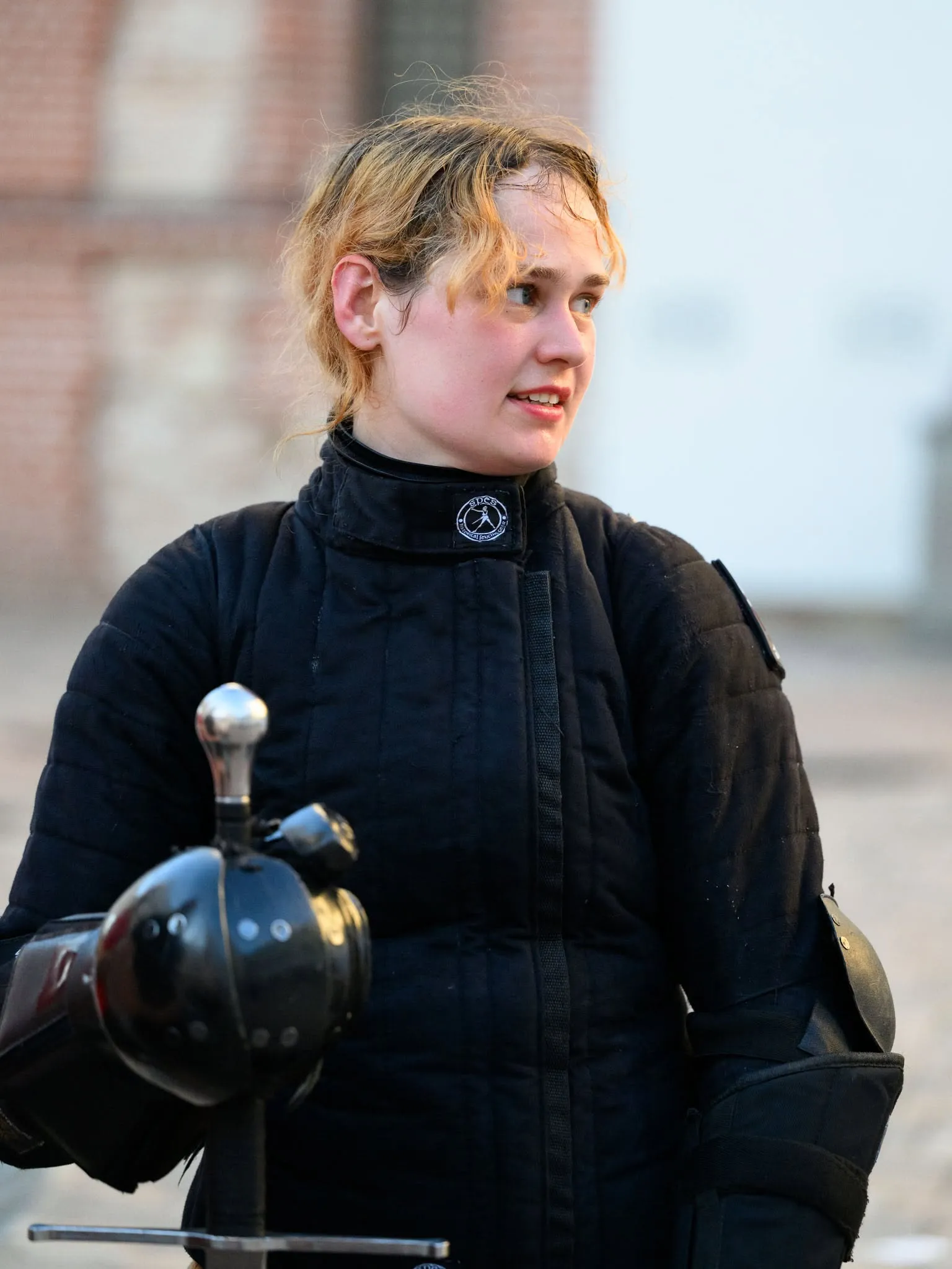 Fencer in a black gambeson waiting for her turn at a tournament