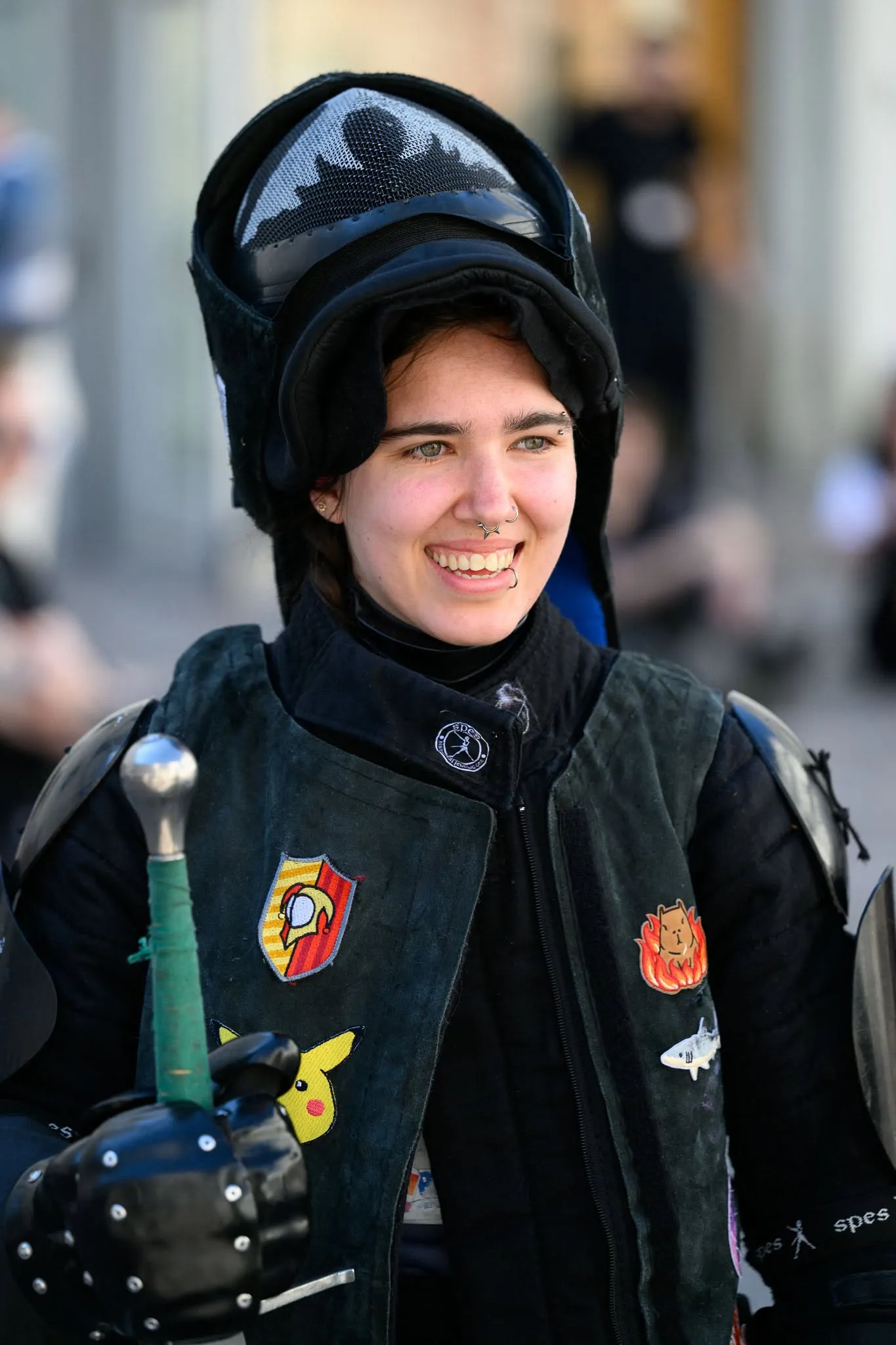 Smiling fencer with a helmet on her head and club patches on her vest