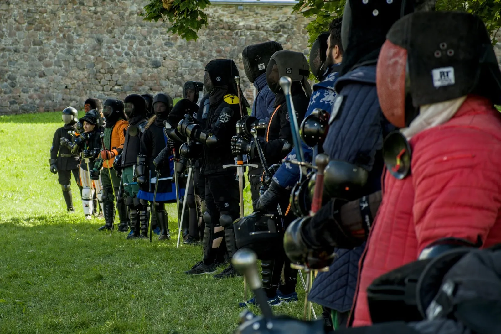 Row of fencers with helmets and swords waiting to fight by a castle wall